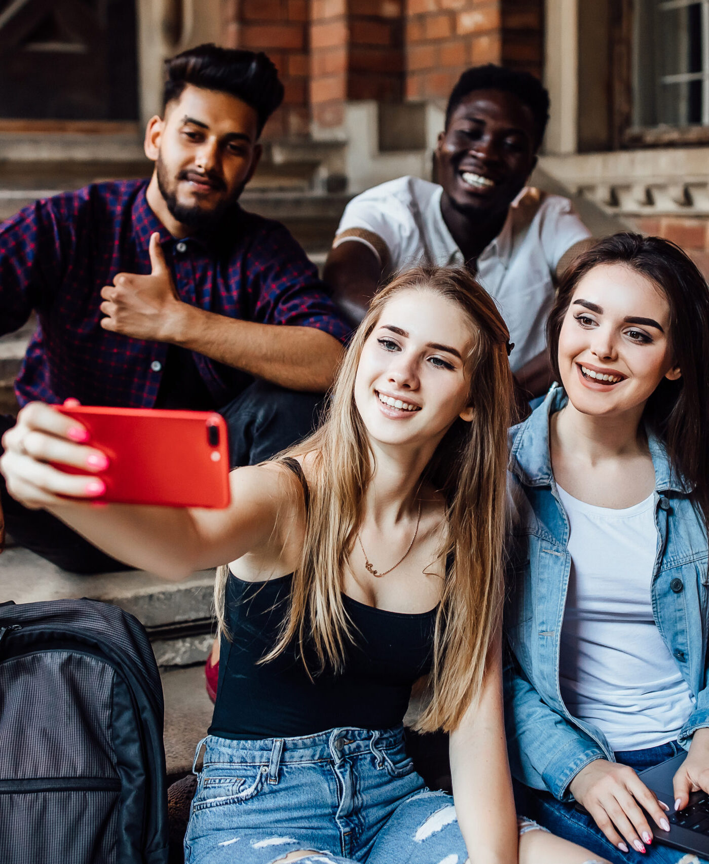 Young blonde woman making selfie with her friends students, while they are sitting on stairs.